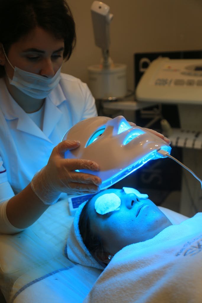 A beautician applying an LED face mask during a relaxing facial treatment in a beauty salon.